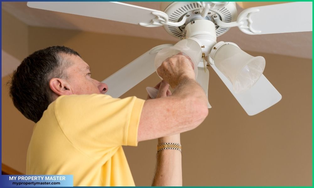 A Man replacing the bulb in ceiling fan and light